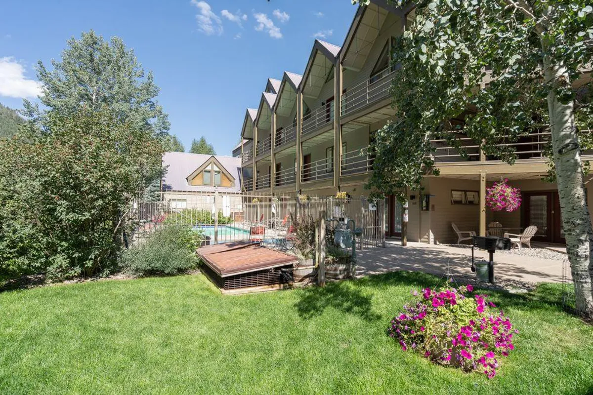 A cheerful scene showcasing the outdoor swimming pool surrounded by colorful flower beds and balconies of the building. People are seen sunbathing by the pool, relaxing outdoors, and socializing on the balconies, underscoring the sense of community.