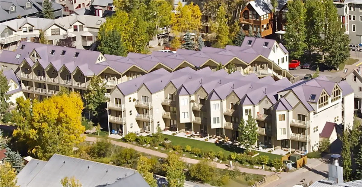Rows of charming buildings with gabled roofs are nestled amidst lush greenery. Balconies with seating areas invite guests to enjoy the fresh mountain air, scenic views, and moments of connection with nature.