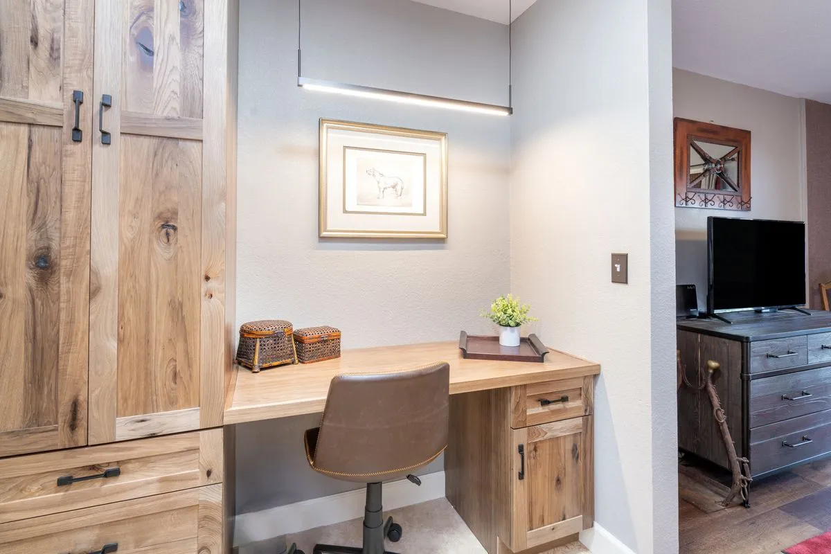 A dedicated interior workstation with a wooden desk, framed artwork above, a potted plant, and a storage cabinet. The space is tidy, well-lit, and designed to encourage productivity in a comfortable setting.