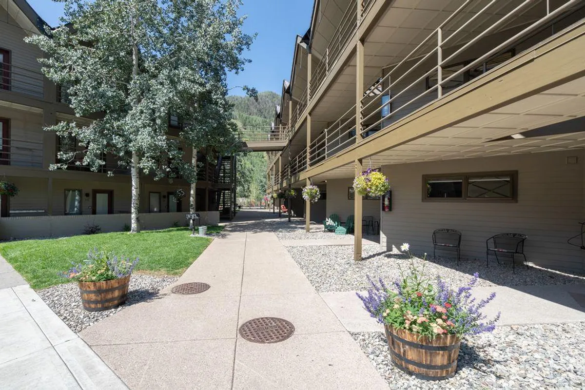 A tranquil courtyard framed by aspen trees and flower planters, with the property's architecture in the background. Seating areas invite guests to relax or socialize outdoors, enhancing the sense of thoughtful amenities and shared spaces.